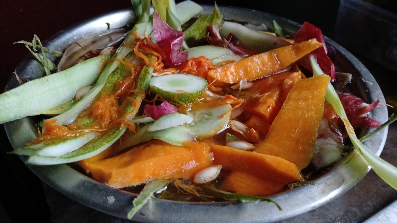 A steel plate of kitchen scraps — cucumber and pumpkin peel, seeds, onion skins and green stalks.
